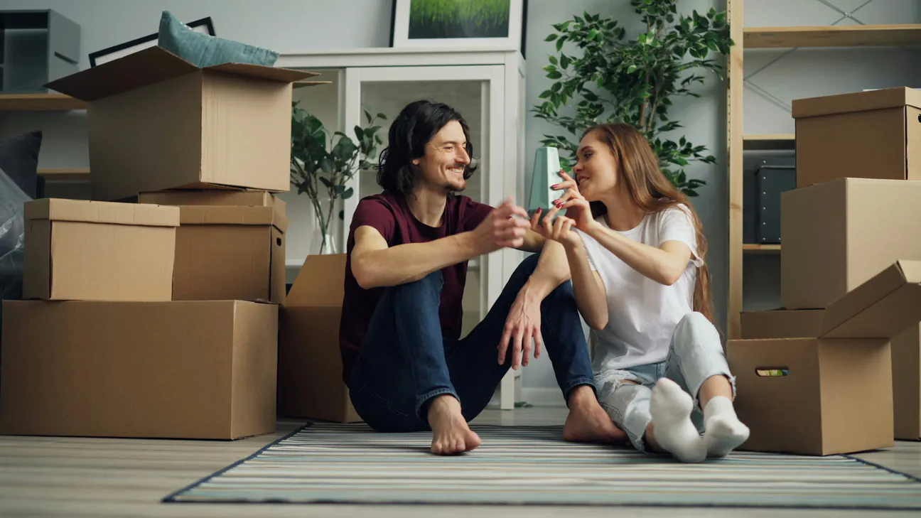 A couple sitting on the floor of their new home among moving boxes, laughing together